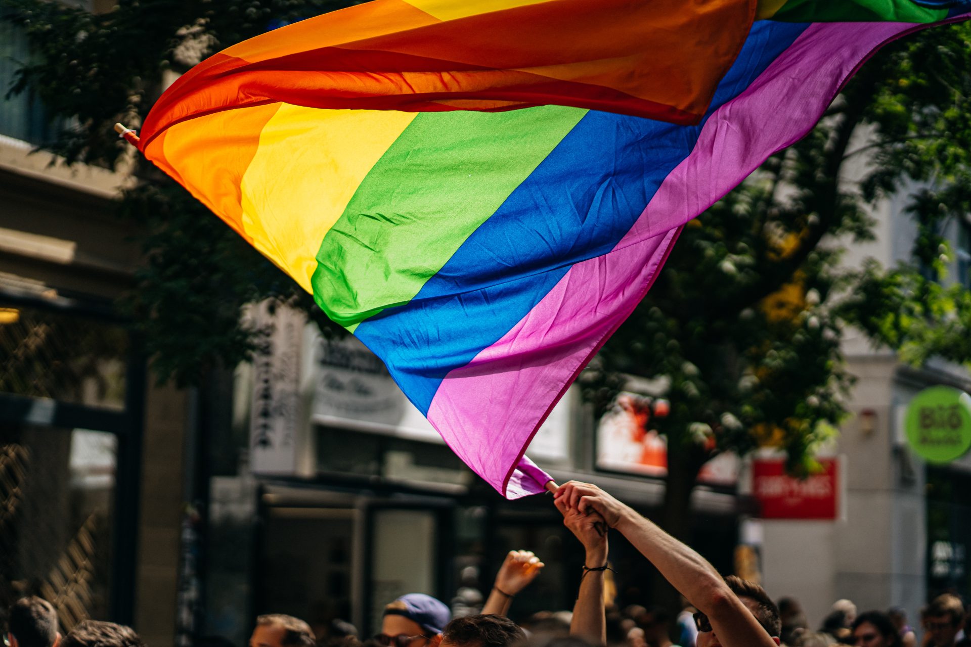 Pride flag being waved above a crowd of people in a street